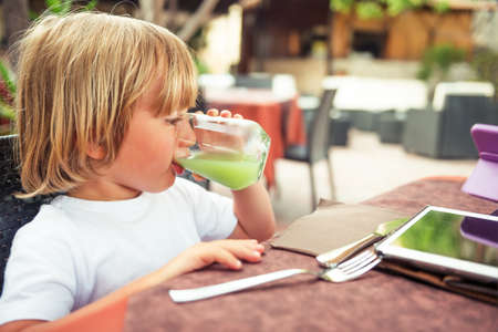 Adorable little boy drinking fresh apple juice in a restaurantの写真素材
