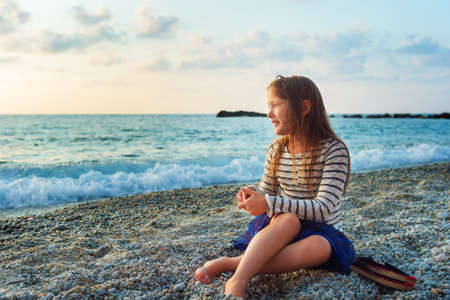 Cute little girl having fun outdoors, resting on the beach at sunsetの写真素材