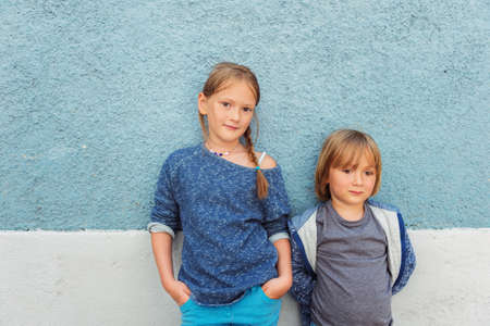 Two kids, girl and little boy, posing outdoors, standing against blue wallの写真素材
