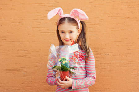 Cute little girl wearing rabbit ears, holding spring flowers in a pot with french sign joyeuses paques - happy easterの写真素材