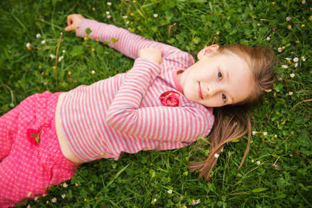 Portrait of a cute little girl of 7 years old in the park, laying on grass, wearing red clothesの写真素材