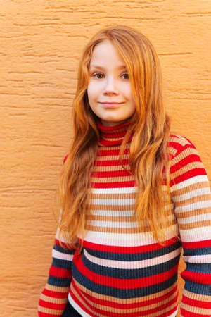 Vertical fashion close up portrait of adorable redheaded girl against orange wall, wearing stripes roll neck pulloverの写真素材