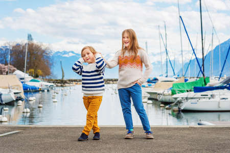 Two adorable kids playing by the lake in early spring, wearing pullovers and colorful trousersの写真素材