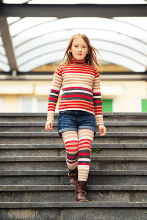 Fashion portrait of a cute little girl in a city, wearing brown boots, denim shorts, stripes rollnecck pullover and tightsの写真素材