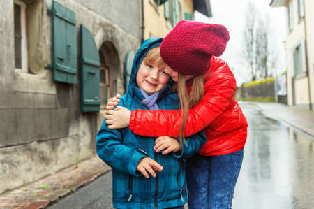 Big sister giving a hug to her small brother, kids wearing bright warm jacketsの写真素材