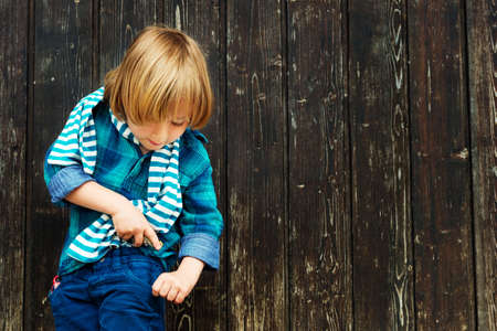 Fashion portrait of a cute little blond boy against wooden background, wearing emerald shirt and...
