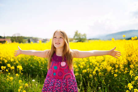 Outdoor portrait of a cute little girl playing with flowers in a countryside, arms wide open
