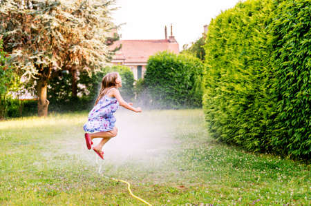 Child playing with garden sprinkler, jumping overの写真素材