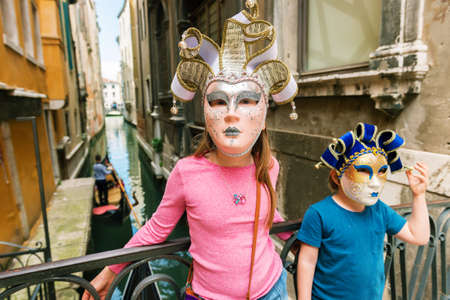 Two kids playing with famous venetian masks. Little girl and boy visiting Venice, Italy. Small tourists wearing souvenir carnival masksの写真素材