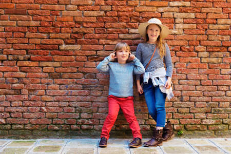 Outdoor portrait of adorable fashion kids, standing against old red brick wallの写真素材