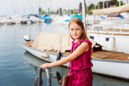 Fashion stylish portrait of pretty preteen girl of 8-9 years old, wearing maroon jumpsuit, posing by the lakeの写真素材