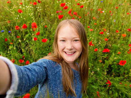 Funny little girl doing selfie in poppy field. Preteen 8-9 years old girl taking photos of herselfの写真素材