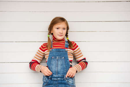 Fashion portrait of a cute little girl against white background, wearing stripe roll neck pullover and denim overallsの写真素材