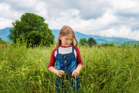 Little girl playing in green wheat field in summertime, wearing red and white t-shirt and overallsの写真素材