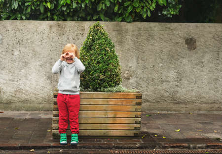 Fashion portrait of adorable toddler boy wearing grey sweatshirt, red trainings and green shoes. Kid pretending taking pictures with his handsの写真素材