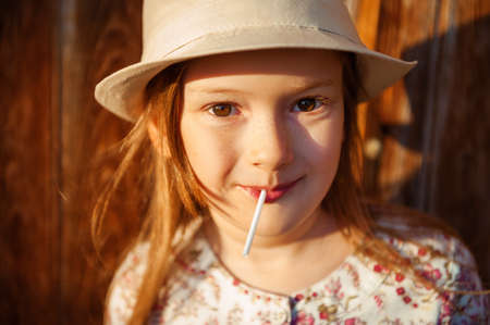 Close up portrait of a cute little girl of 6-7 years old with lollipop at sunsetの写真素材