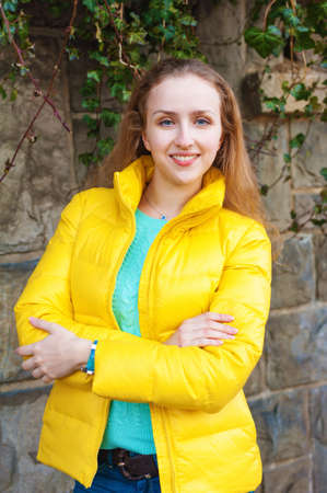 Outdoor portrait of a young woman wearing bright yellow jacket, vertical image