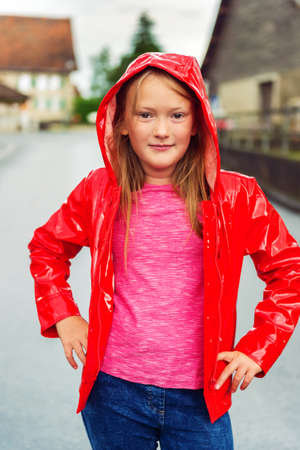 Vertical outdoor portrait of a cute little girl of 8-9 years old on a cloudy day, wearing bright red rain jacketの写真素材