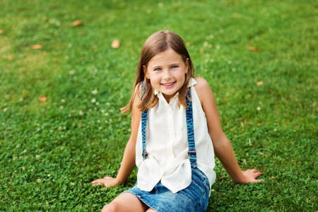 Portrait of a cute little girl 7-8 year old in the park, sitting on grassの写真素材