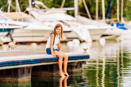 Cute little kid girl resting by the lake, sitting on pierの写真素材