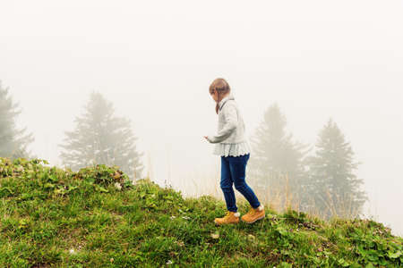 Cute little girl of 8 years old playing outdoors on a very foggy day, wearing grey warm pulloverの写真素材