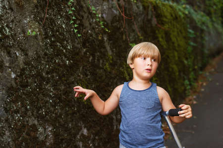 Portrait of adorable young 4 years old blond boy leaning on his scooter