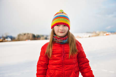 Little girl wearing red jacket and colorful hat, playing with snow in winter timeの写真素材
