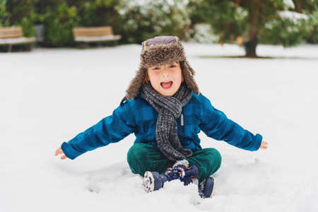 Cute little boy playing in winter park. Kid having fun outdoors, running on snow, wearing warm blue...