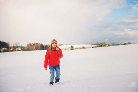 Little girl wearing red jacket and colorful hat, playing with snow in winter timeの写真素材