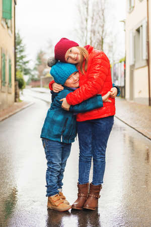 Big sister giving a hug to her small brother, kids wearing bright warm jacketsの写真素材