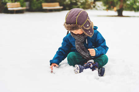 Cute little boy playing in winter park. Kid having fun outdoors, running on snow, wearing warm blue jacket, hat and scarfの写真素材