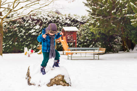 Cute little boy playing in winter park. Kid having fun outdoors, running on snow, wearing warm blue jacket, hat and scarfの写真素材