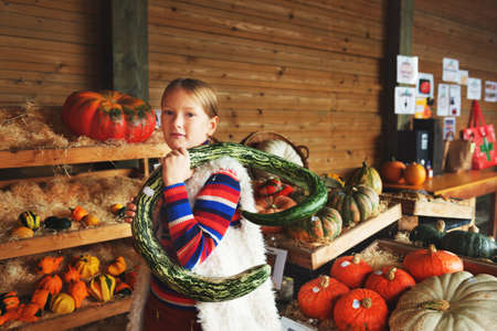 Adorable little girl of 8-9 year old choosing halloween pumpkin on farm market, having fun with unusual different kind of pumpkinsの写真素材