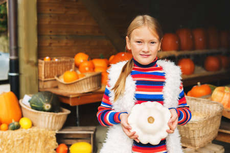 Adorable little girl of 8-9 year old choosing halloween pumpkin on farm market, holding white squashの写真素材