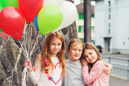 Outdoor portrait of 3 cute little girls with colorful balloons, wearing sweatshirtsの写真素材
