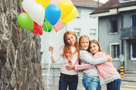 Outdoor portrait of 3 cute little girls with colorful balloons, wearing sweatshirtsの写真素材