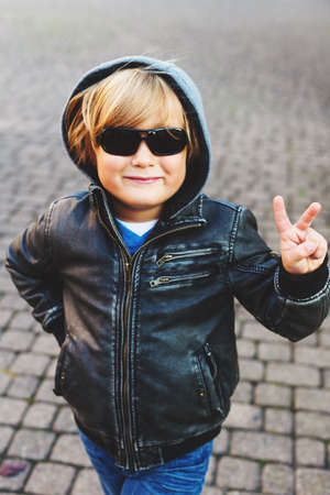 Outdoor portrait of adorable little blond boy wearing black leather jacket and sunglassesの写真素材
