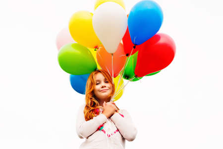 Happy little 8-9 year old girl with red hair holding colorful helium balloonsの写真素材