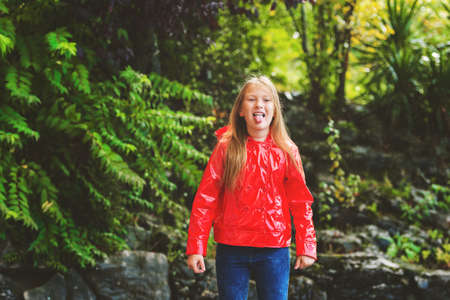 Adorable little girl catching rain drops with her tongue, wearing red rain coatの写真素材