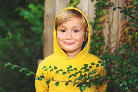 Outdoor portrait of adorable little 5 year old blond boy playing in the park, wearing yellow sweatshirt with hoodの写真素材