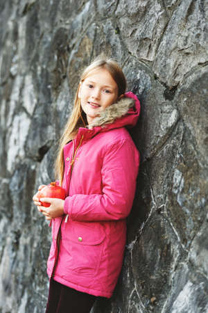 Outdoor vertical portrait of cute 9 year old little girl wearing pink winter coat in a city, holding pomegranateの写真素材