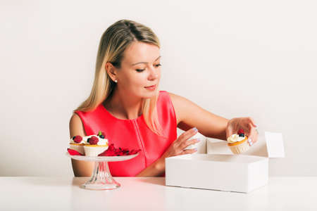 Beautiful young blond woman putting fresh home made cupcakes in white boxの写真素材