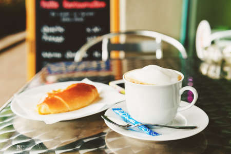Cup of coffee and vanilla bread on table in cafeの写真素材