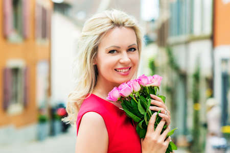 Outdoor portrait of beautiful blond woman holding bouquet of pink rosesの写真素材