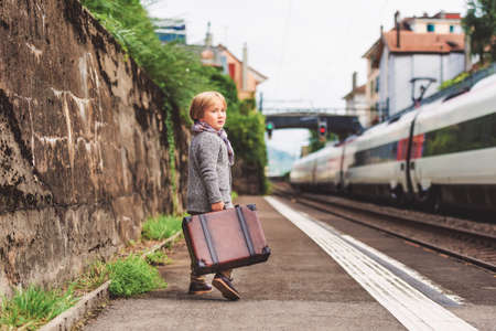 Adorable little boy on a railway station, waiting for the train with suitcaseの写真素材