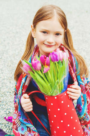Spring close up portrait of 7 year old girl holding polka dot watering can with fresh pink tulips