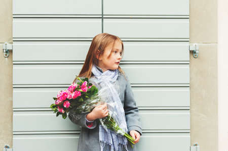 Outdoor portrait of 5-6 year old little girl wearing grey coat and scarf, holding bouquet of pink rosesの写真素材