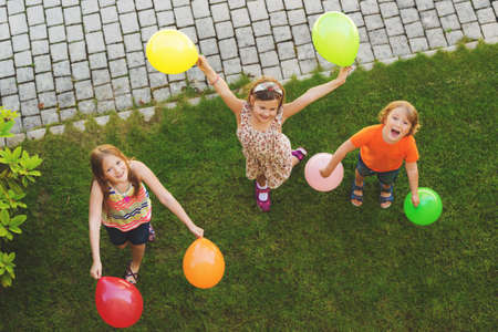 Three happy little kids playing with colorful balloons outdoors, top viewの写真素材