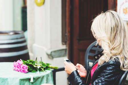 Young blond woman using cell phone, resting in cafe, back viewの写真素材