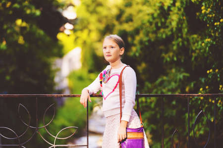 Fashion portrait of a cute little girl outdoors, wearing white sweatshirt with heart and purple bagの写真素材